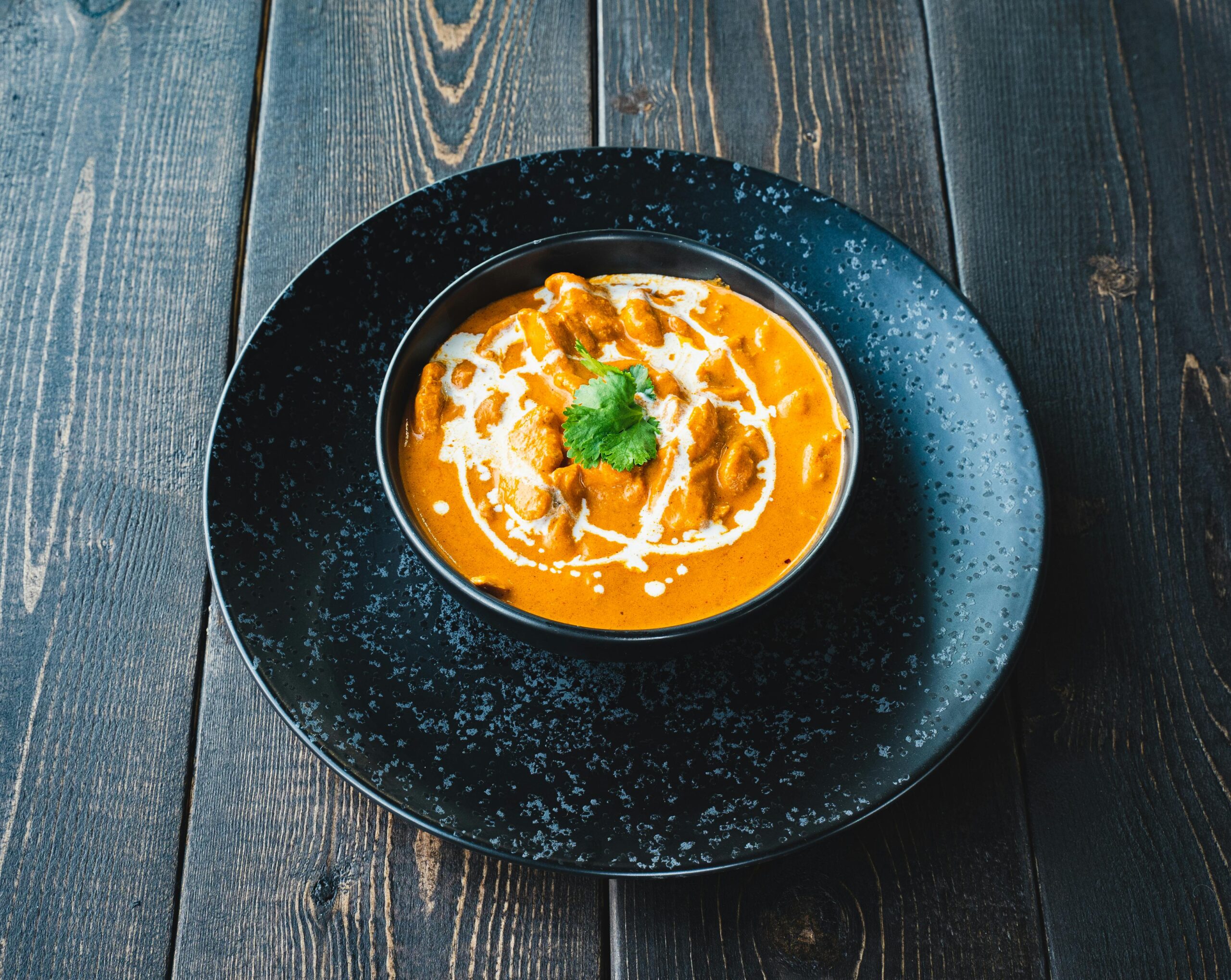 Aromatic creamy curry in a ceramic bowl on a rustic wooden table, topped with cilantro.