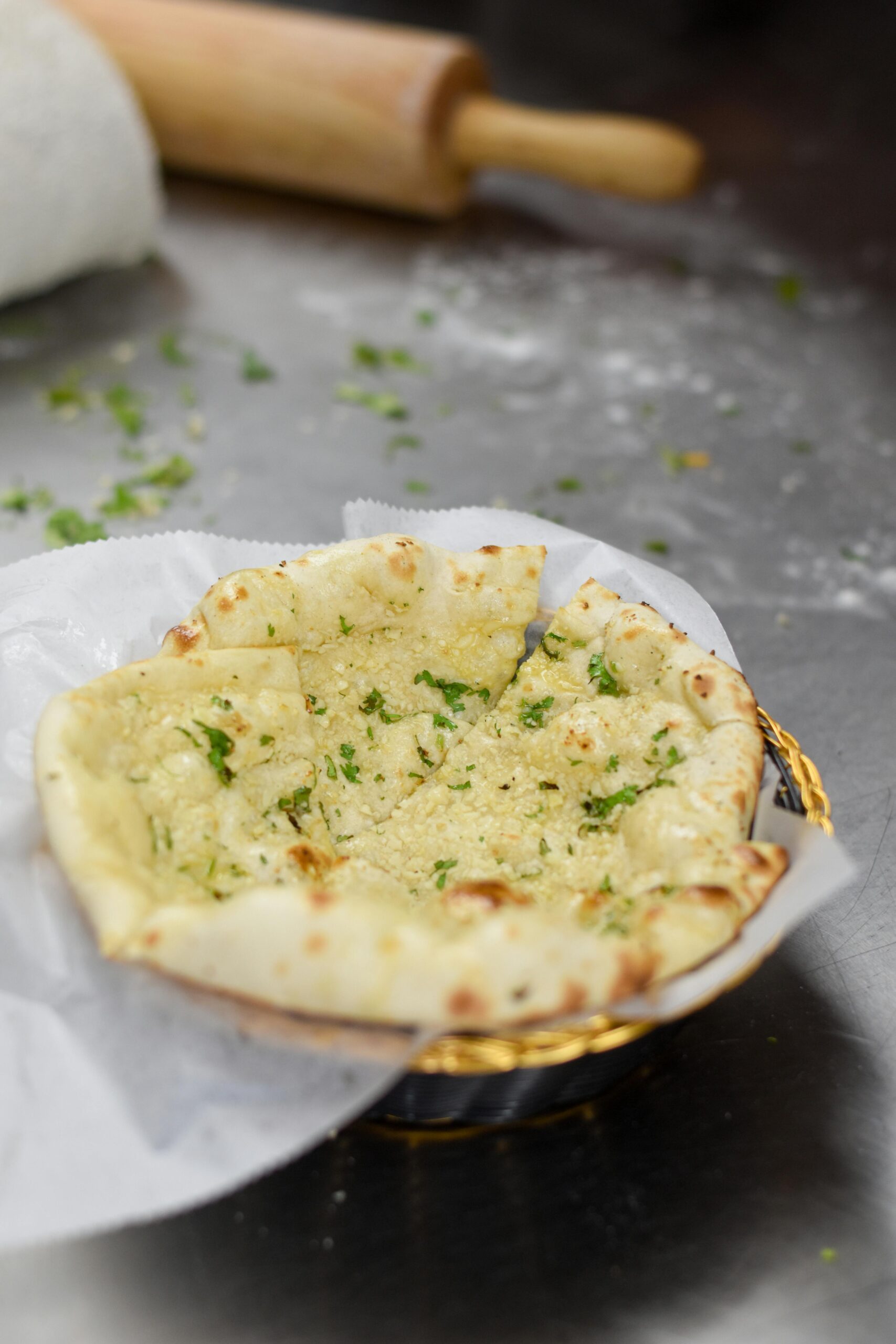 Close-up shot of freshly made garlic naan bread with herbs on a kitchen surface.