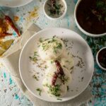 Top view of delicious Idli rice cakes with herbs and spicy tomato soup served on table near sauces and scattered spices
