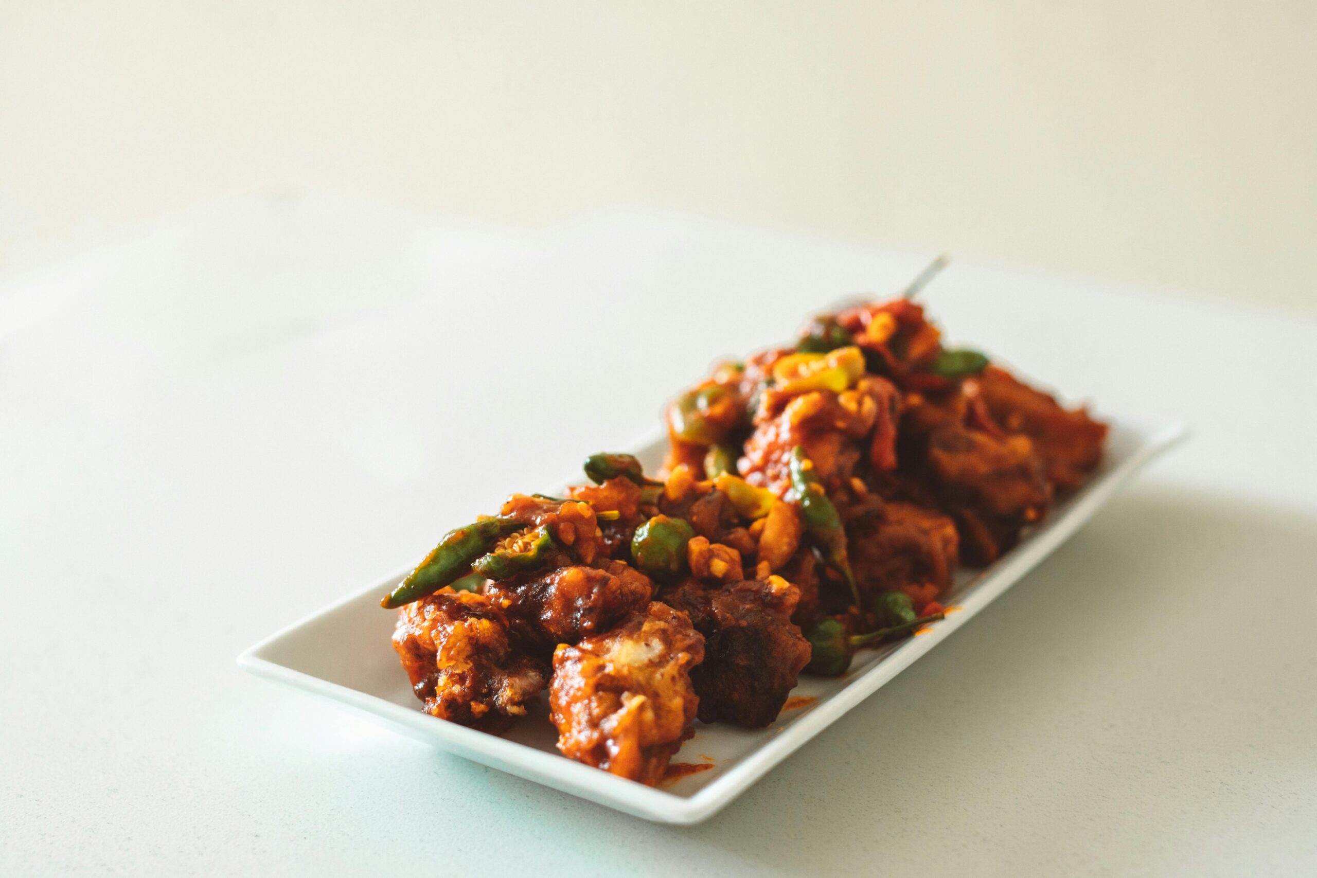 Close-up of spicy chicken Manchurian curry garnished with green peppers on a white dish.