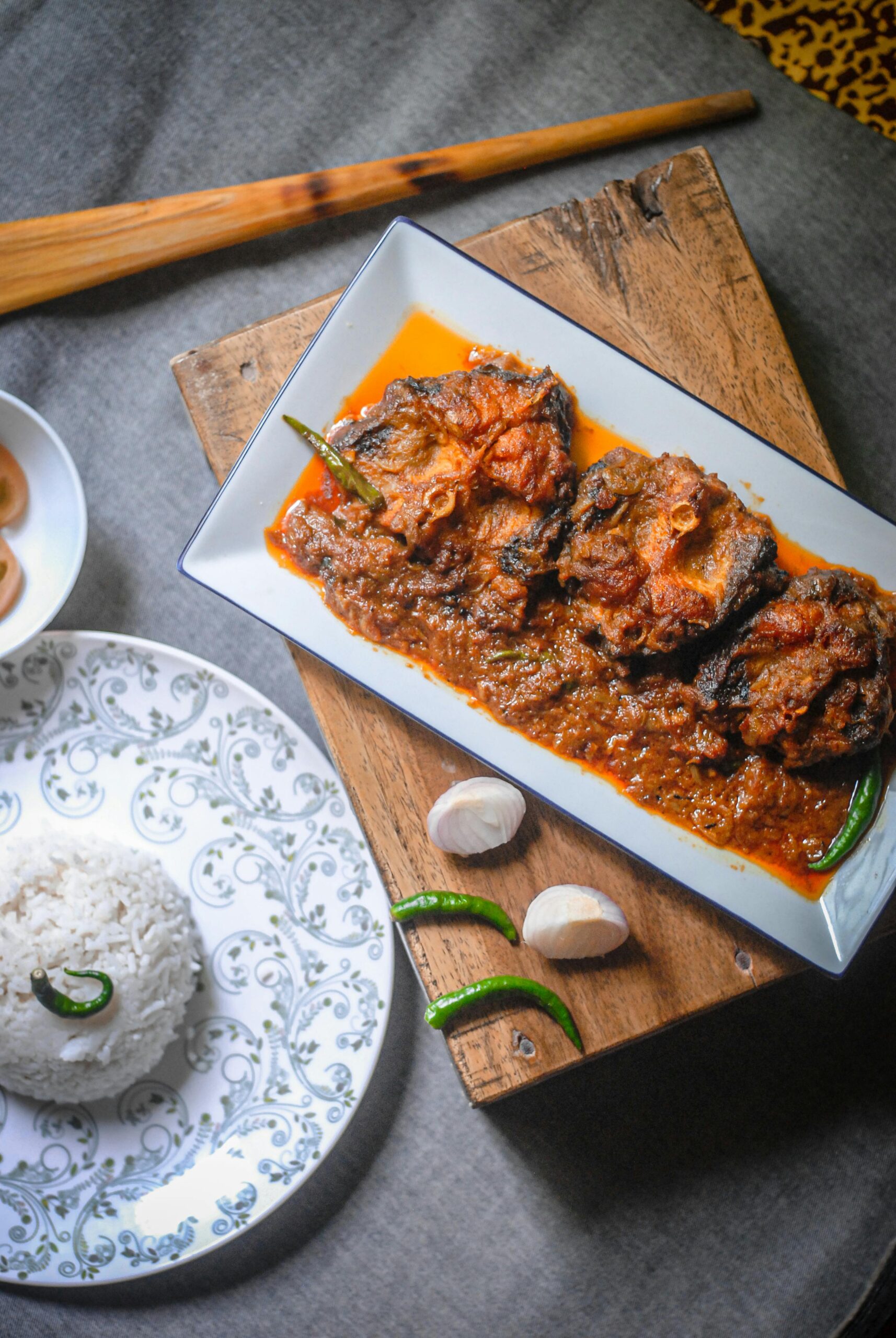Top view of a spicy fish curry served with rice and fresh garlic on a wooden table.